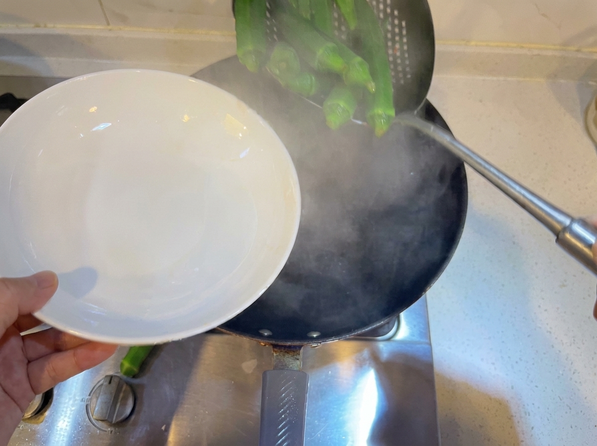 熱湯の入った鍋の中で、穴あきお玉を使って丸ごとの緑のオクラが茹でられている様子。