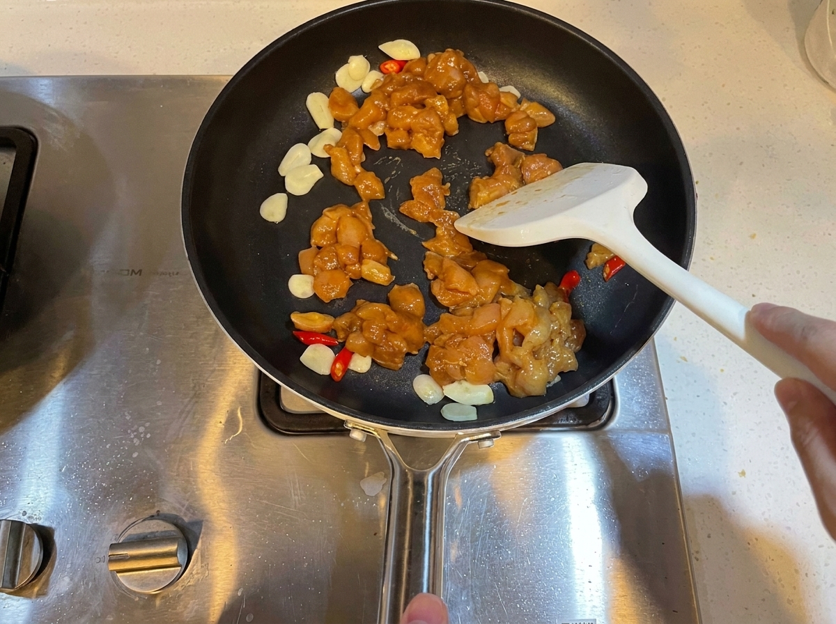ニンニクと唐辛子と一緒に、下味をつけた角切り鶏肉のピースがフライパンで炒められているところ。