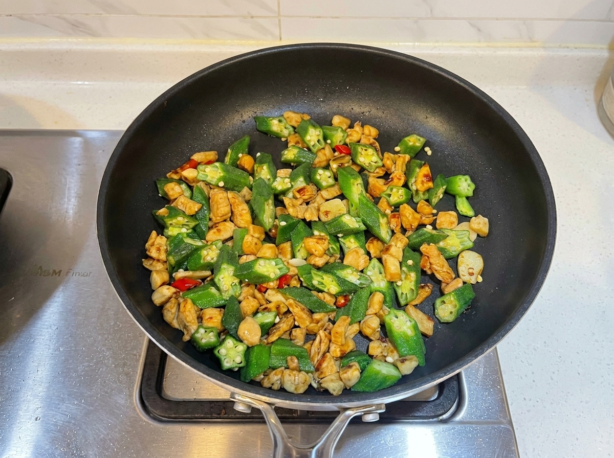 フライパンで炒められている鶏肉とオクラの炒め物に、オイスターソースが加えられているところ。