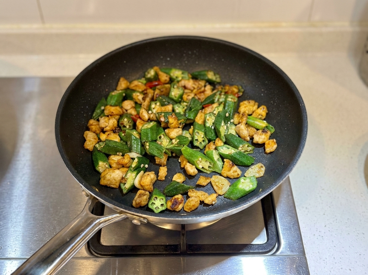 少し水分が飛んで、すぐにでも食べ頃に見える完成した鶏肉とオクラの炒め物がフライパンに入っている様子。