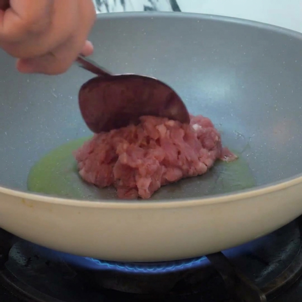 熱した油を入れたフライパンにひき肉が加えられ、炎の上で炒められている様子。