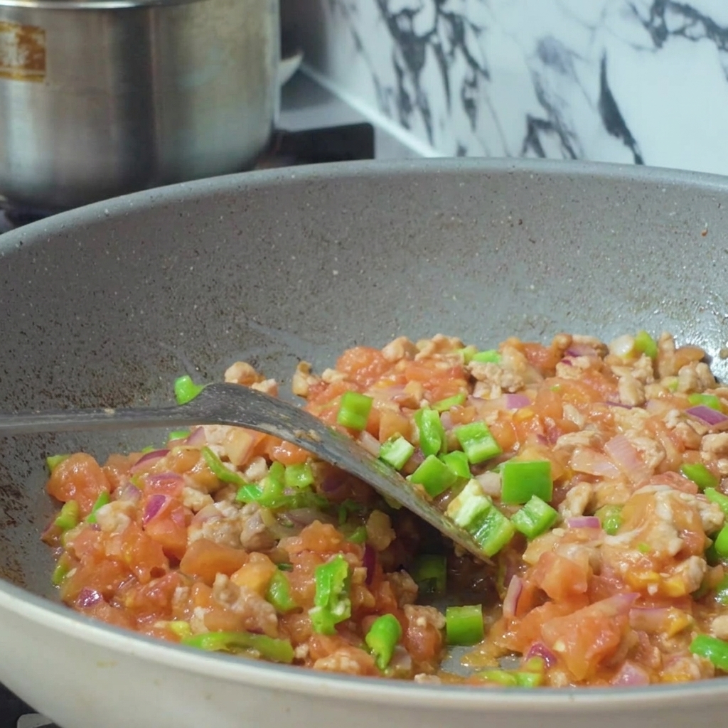 ひき肉と刻み野菜が入ったフライパンに、容器から水が注がれている様子。