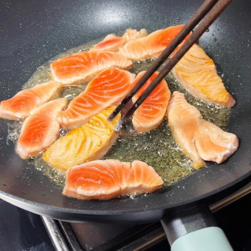 熱したフライパンの中で、きつね色に焼けたサーモンの切り身を木製の箸で優しく裏返しているところ。