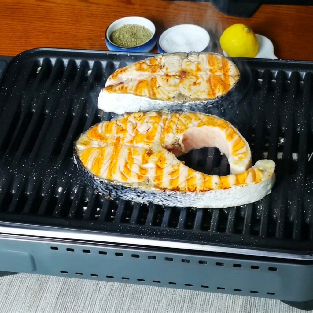 味付けされた後、グリルパンの上でジュージューと音を立てて焼ける鮭のクローズアップ。