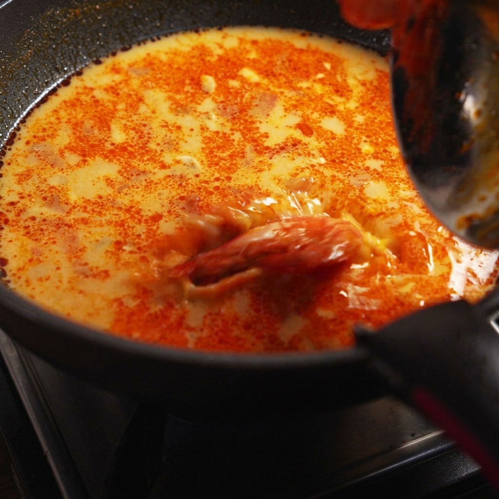 茹でたスパゲッティの麺、海老、フレッシュなパクチーを、ソースの煮立つフライパンに和えている様子。