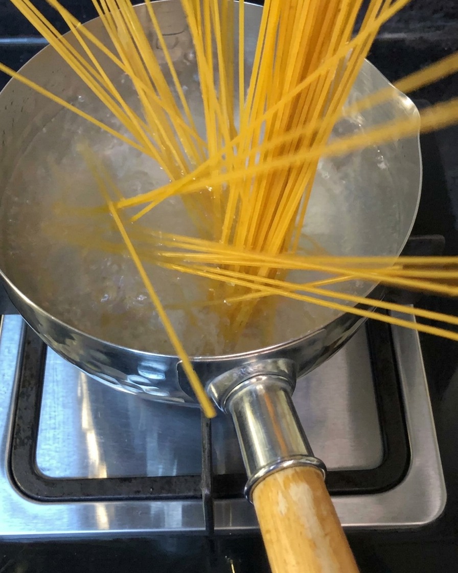 コンロの上の沸騰した塩水が入った鍋にスパゲッティを入れている様子。