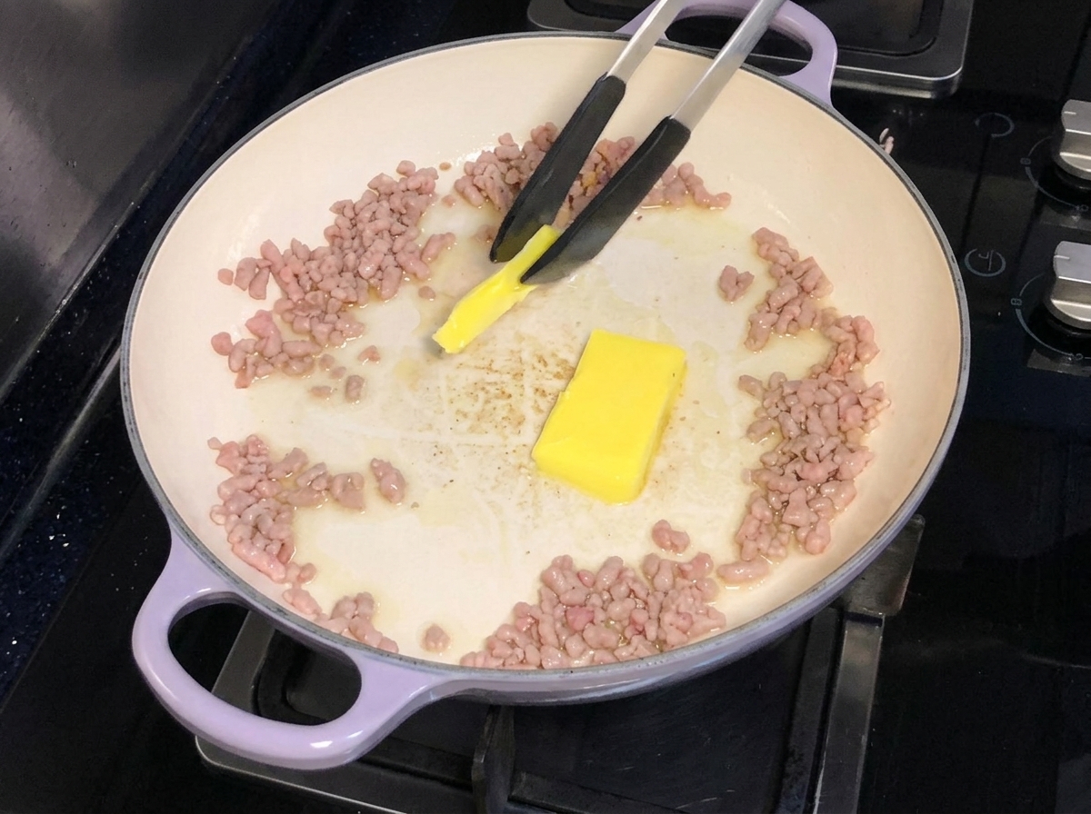 こんがりと炒めた豚ひき肉が入ったフライパンに、バターを加えて溶かしている様子。