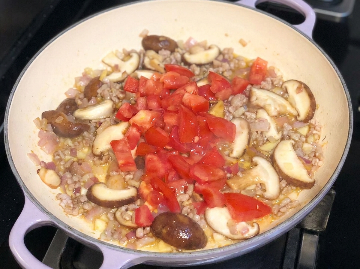 豚肉、玉ねぎ、椎茸を炒めた具材の上に、角切りにしたフレッシュトマトをのせている様子。
