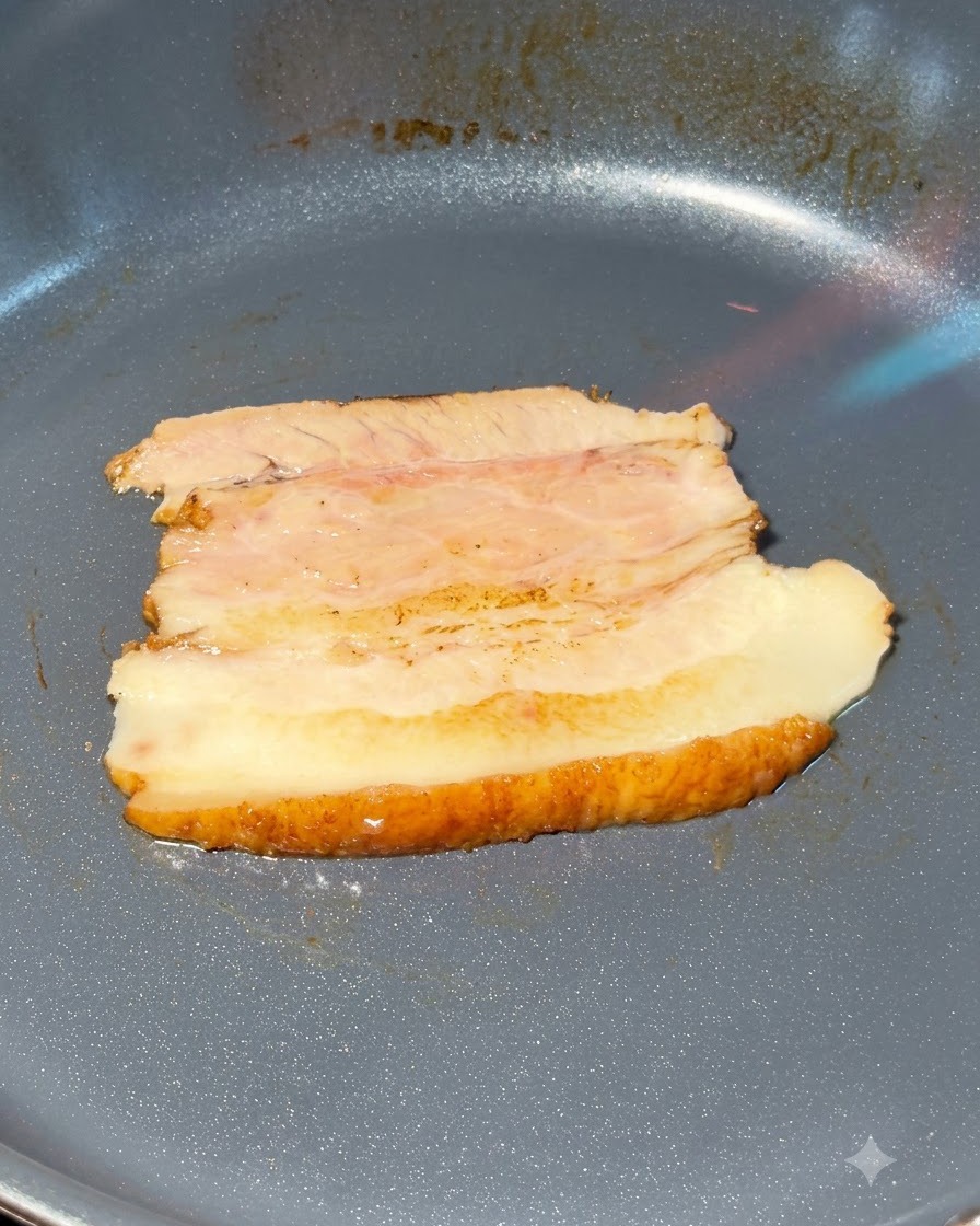 フライパンの上で豚バラチャーシューのスライスをガスバーナーで炙っている様子。