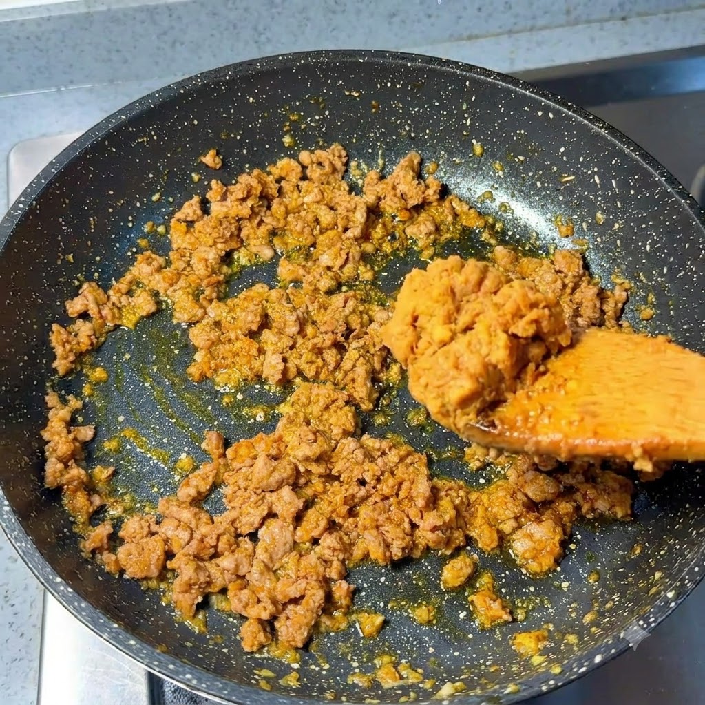 炒めた豚ひき肉が入ったフライパンに、スプーン一杯の味噌を加えているところ