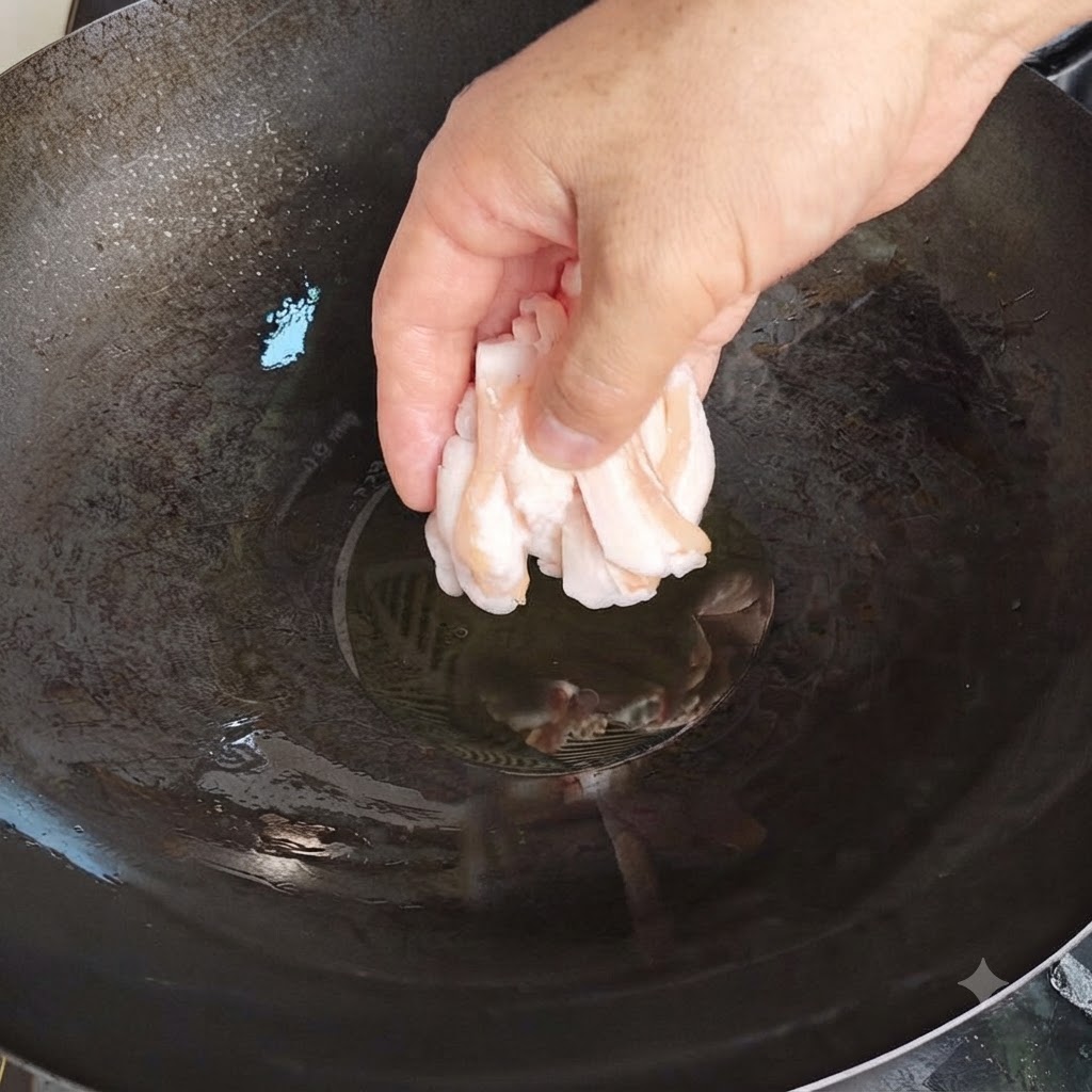 熱した中華鍋に、少量の油と一緒に薄切りにした生の豚脂を手で丁寧に投入している様子。
