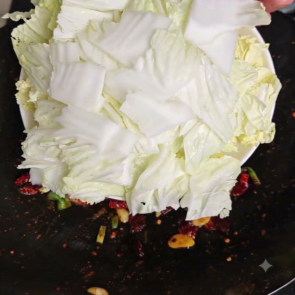 白い皿から、新しく刻んだ生の白菜を熱い中華鍋へ一気に流し込んでいる様子。