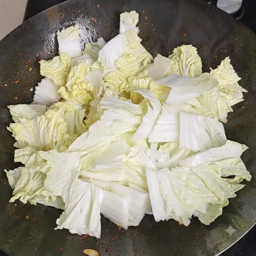 熱い中華鍋の中にある山盛りの新鮮な白菜の上に、塩が均等に振りかけられている様子。