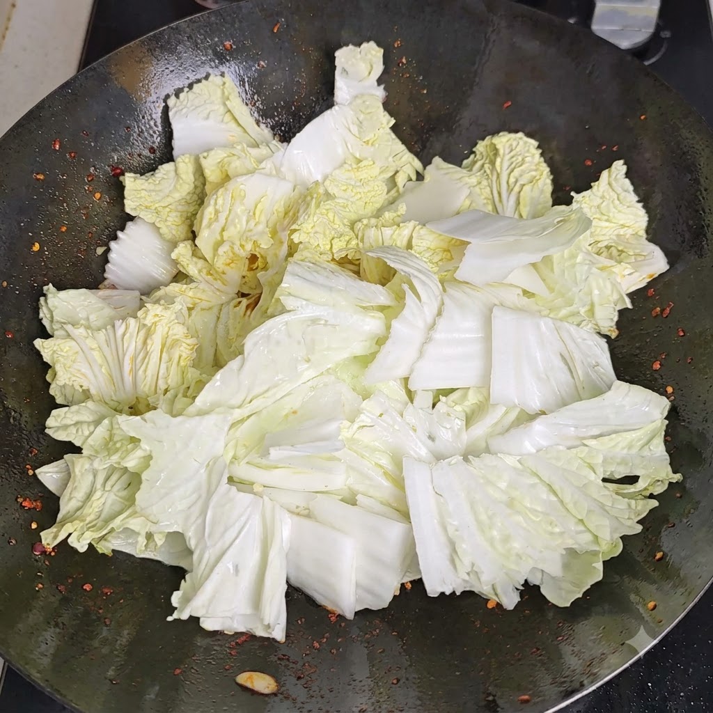 熱せられた中華鍋の縁に沿って酢が注がれ、高温の表面と反応して湯気が立っている様子。