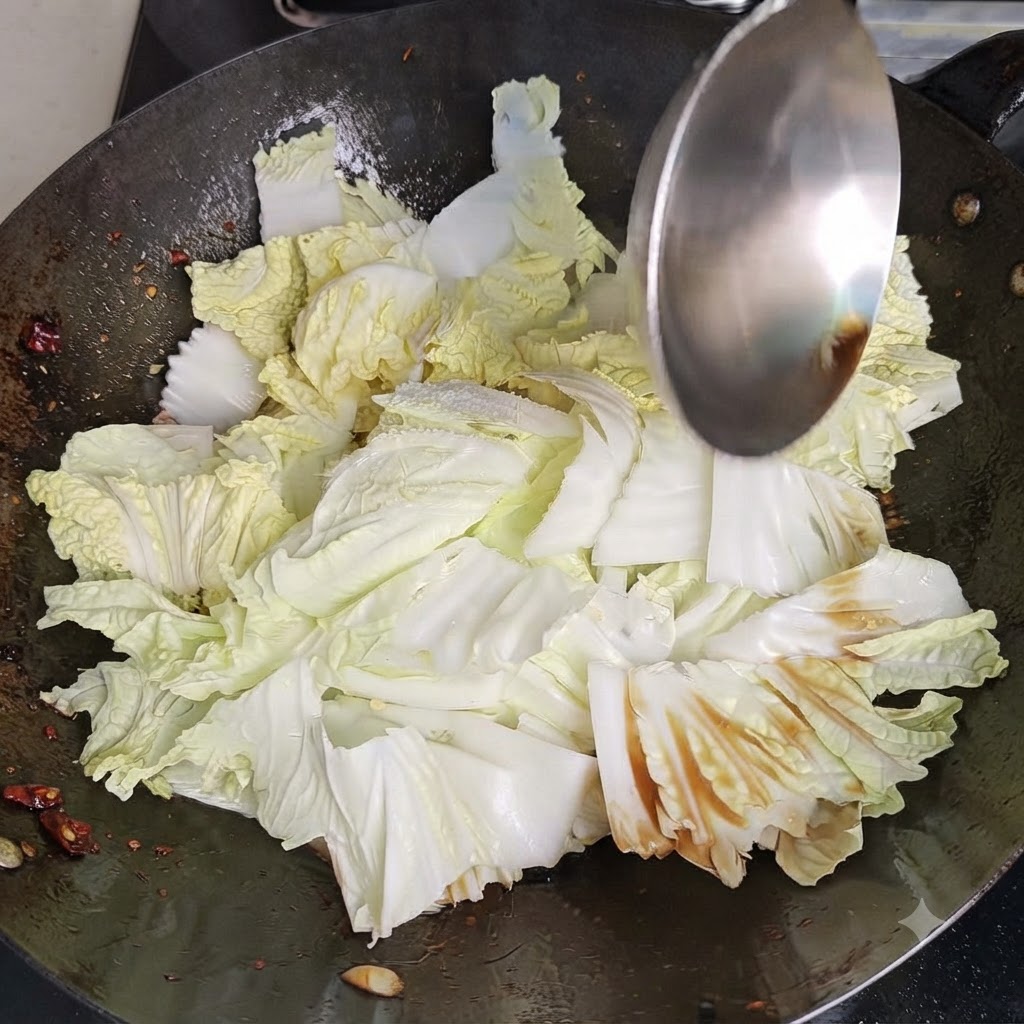 熱い中華鍋の中で、金属製のヘラを使って白菜と調味料を激しくあおり、炒め合わせている様子。