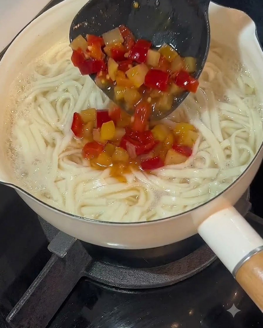 茹で上がった麺の入った鍋の上に、お玉で漬物と唐辛子のスープベースが注がれている様子。