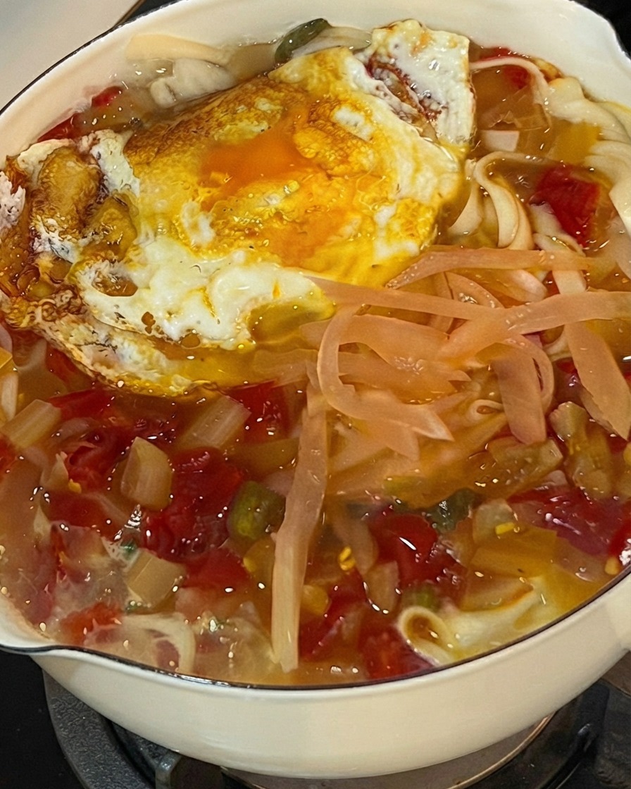 麺、白菜漬け、目玉焼きが入ってグツグツ煮える鍋の上に、刻んだフレッシュなパクチーが振りかけられている様子。