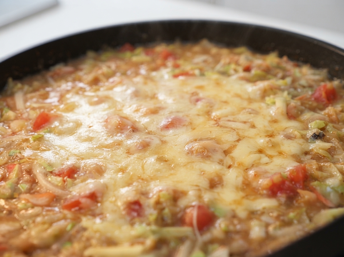 熱いフライパンの上で、泡立つ生地と野菜の上にピザ用チーズがとろけている様子。