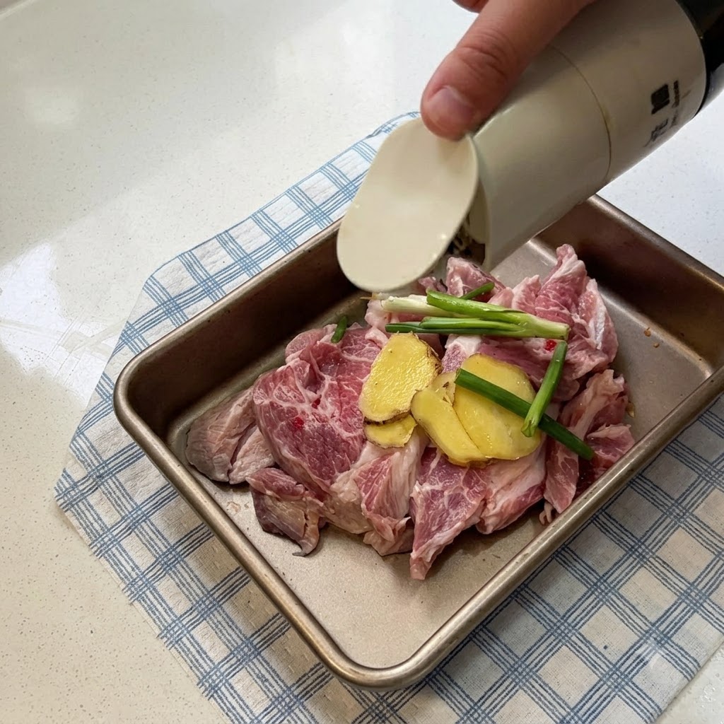 金属製のトレイに並べられた豚肉に、生姜のスライスと青ネギが添えられ、醤油がかけられている様子。