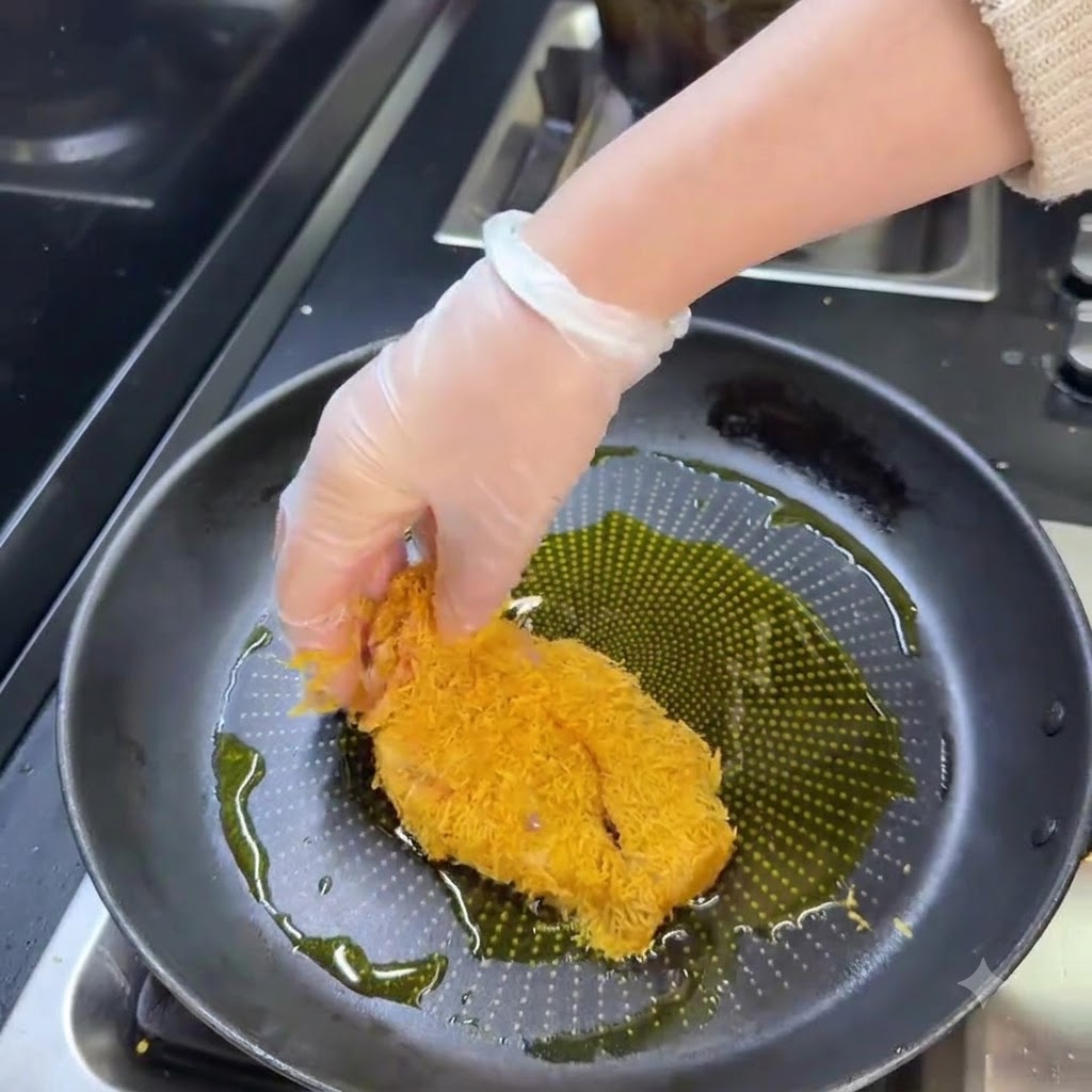 熱した油の入ったフライパンの中で、黄金色になるまで揚げられている衣つきの豚カツ。