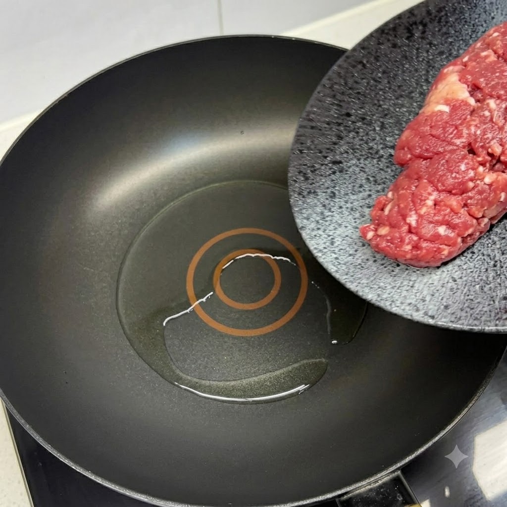 赤いヘラを使い、油を熱した黒いフライパンに新鮮な牛ひき肉を入れているところ。
