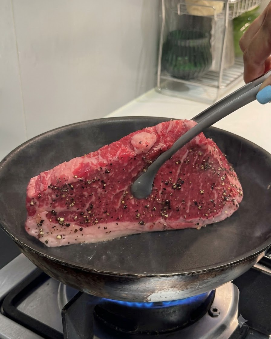 トングでステーキを熱したフライパンに垂直に持ち上げ、端を焼いている様子