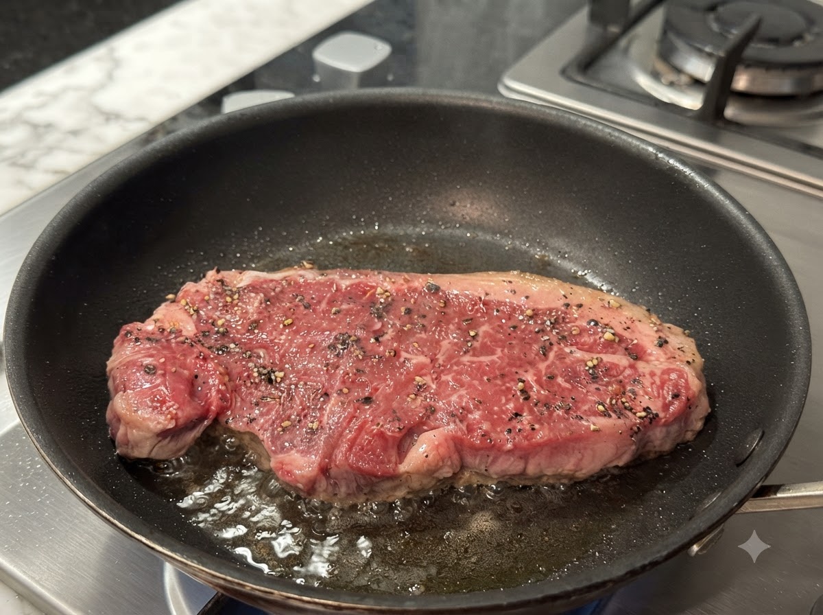 熱したフライパンの中でステーキが焼かれており、表面に香ばしい焼き色がつき始めている様子