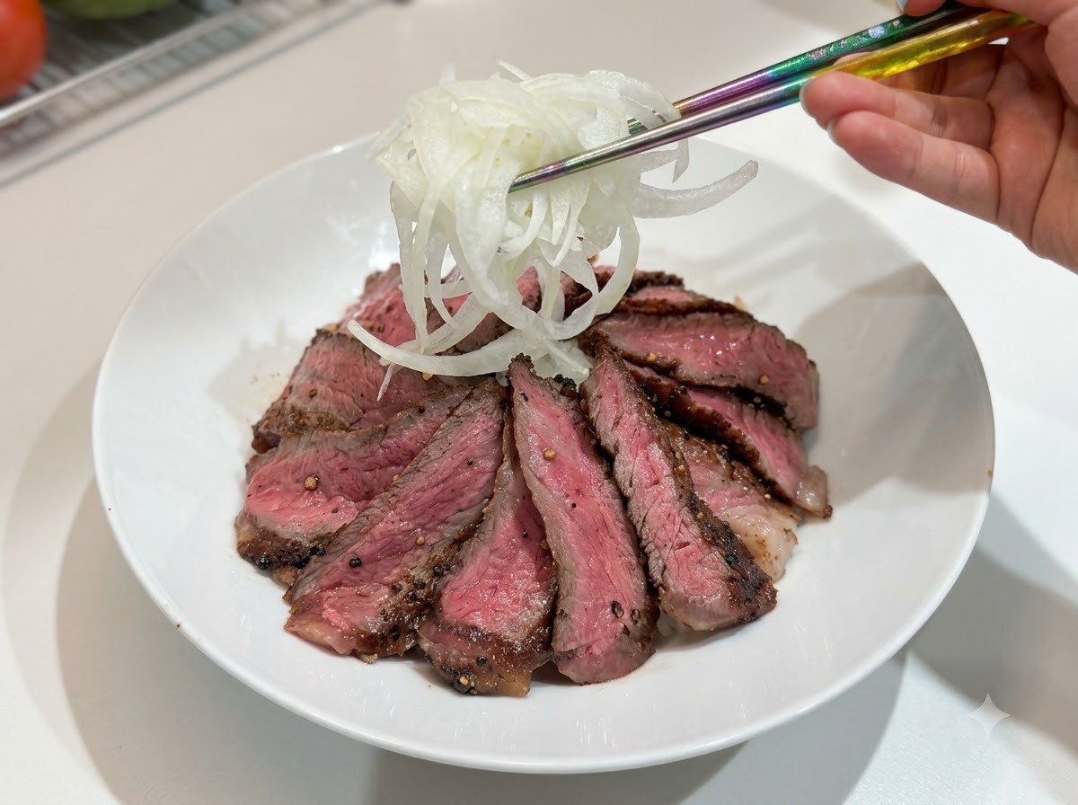 箸を使って、ステーキとご飯の丼に千切り玉ねぎを盛り付けている様子