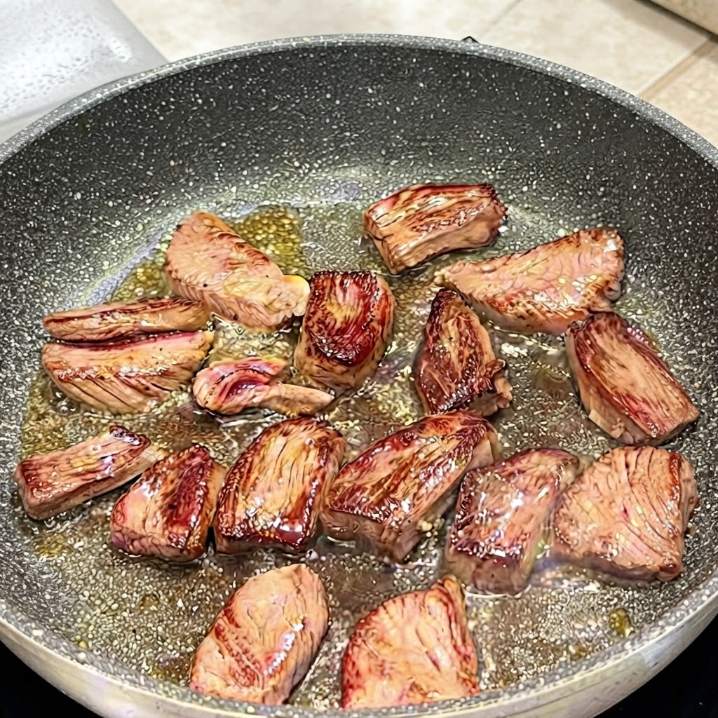 トングを使ってフライパンの中のスカートステーキを裏返し、きつね色に焼けた面を見せている様子。