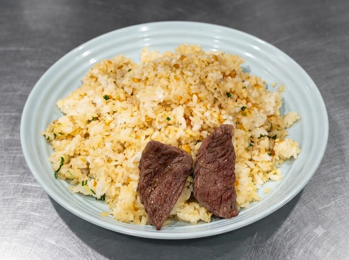 青いお皿に盛られた味付けご飯の上に、トングを使って焼いたステーキ肉をきれいに並べている様子。