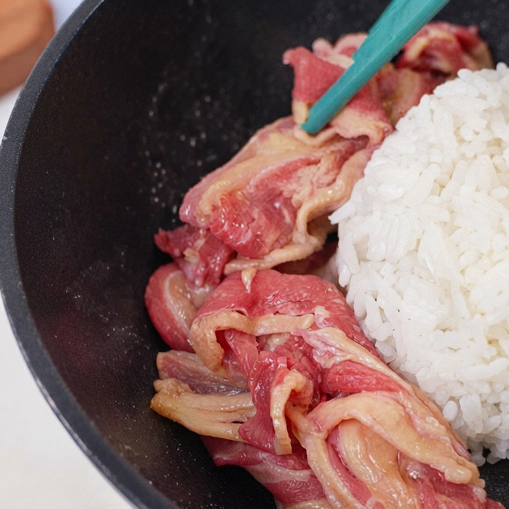 フライパンの中央にあるご飯の周りに、生の牛肉の薄切りを円状に並べている様子。