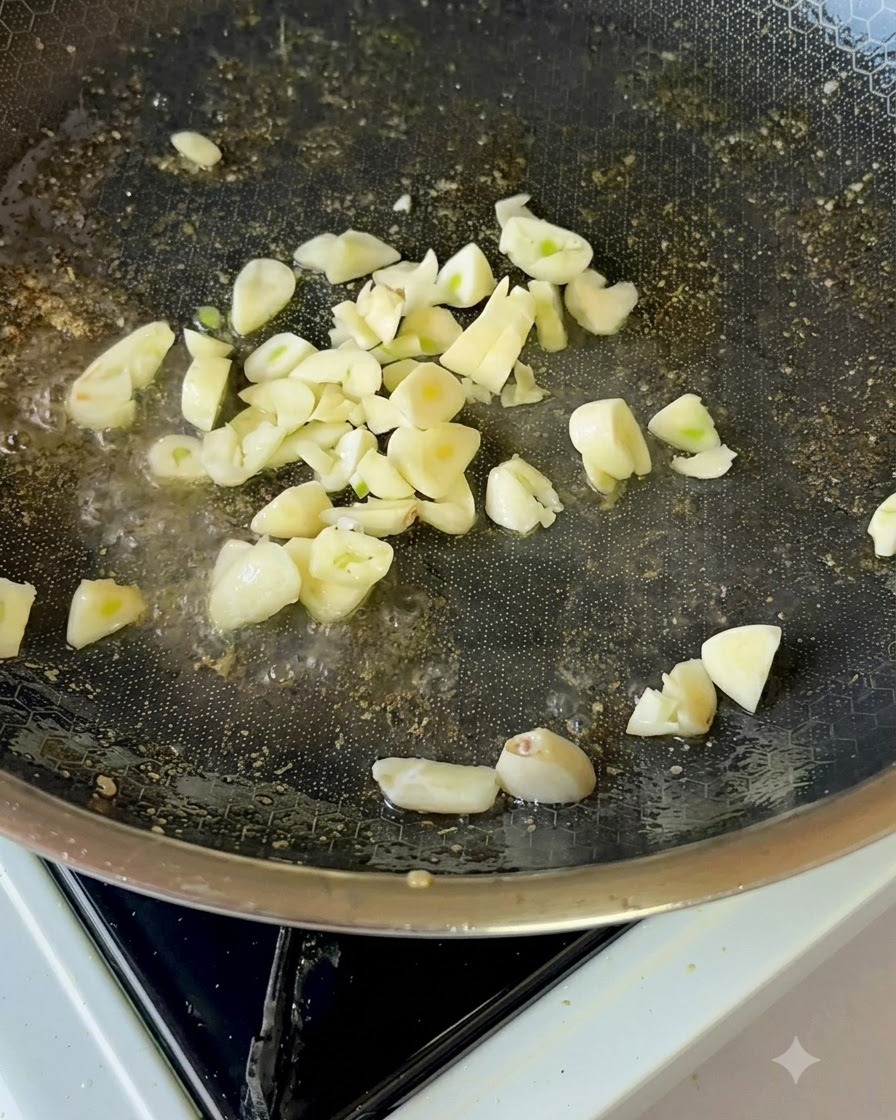 ノンスティックフライパンの中で、薄切りにしたフレッシュなにんにくが油で軽く揚げられている様子。