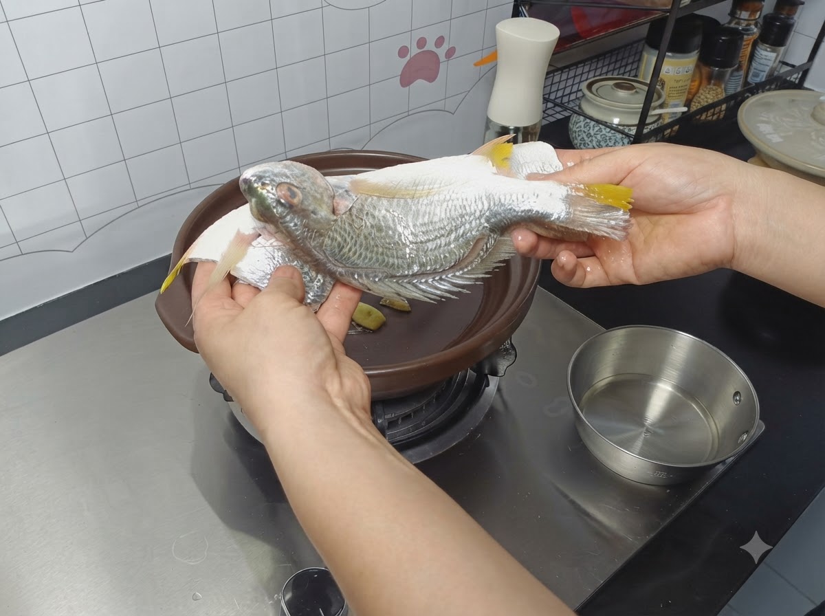 生姜のスライスを敷いた土鍋に、下味をつけた丸ごとの魚を入れている様子。