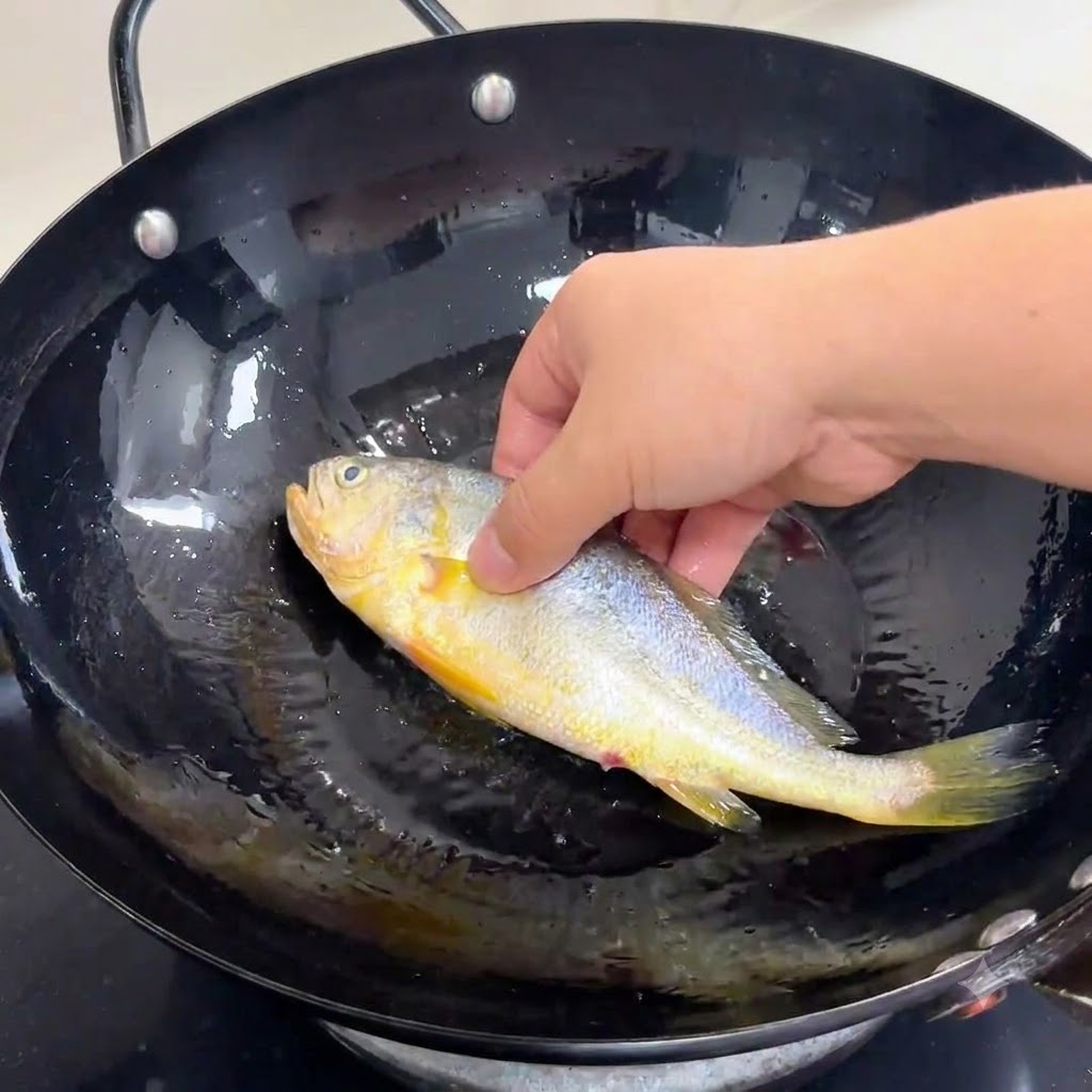 熱した油を入れた黒い中華鍋に、下味をつけた丸ごとの魚を優しく置いている様子。