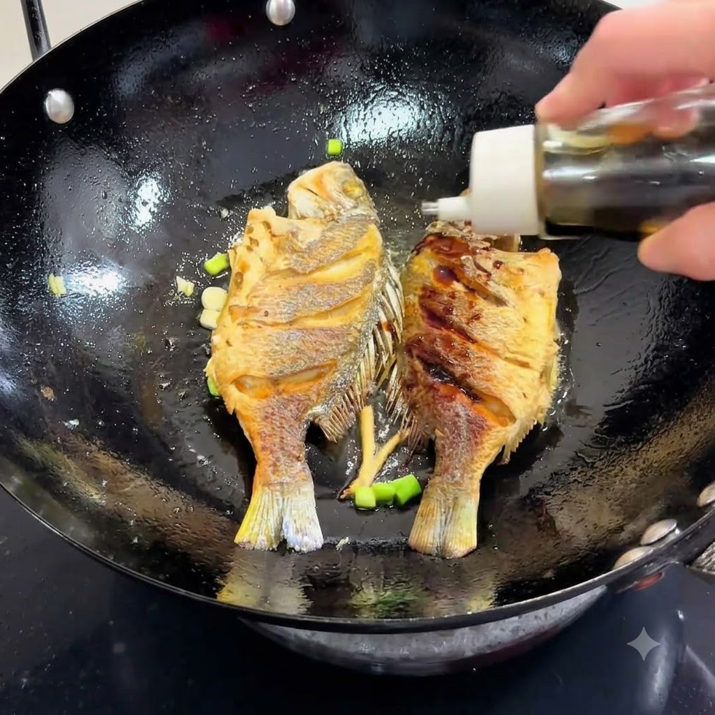 魚とネギが入った中華鍋に、ボトルから醤油が回し入れられている様子。