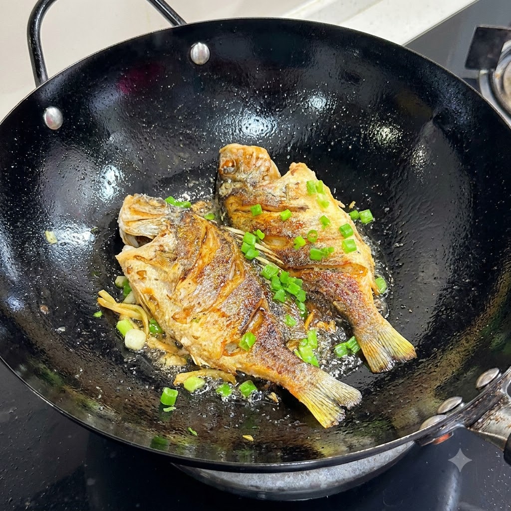 黒い中華鍋の中の黄金色に焼けた魚の上に、刻みネギが均等に振りかけられている様子。