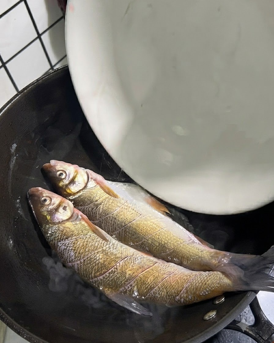 油の入った熱い中華鍋の中に、生のいとより鯛を2匹入れている様子。