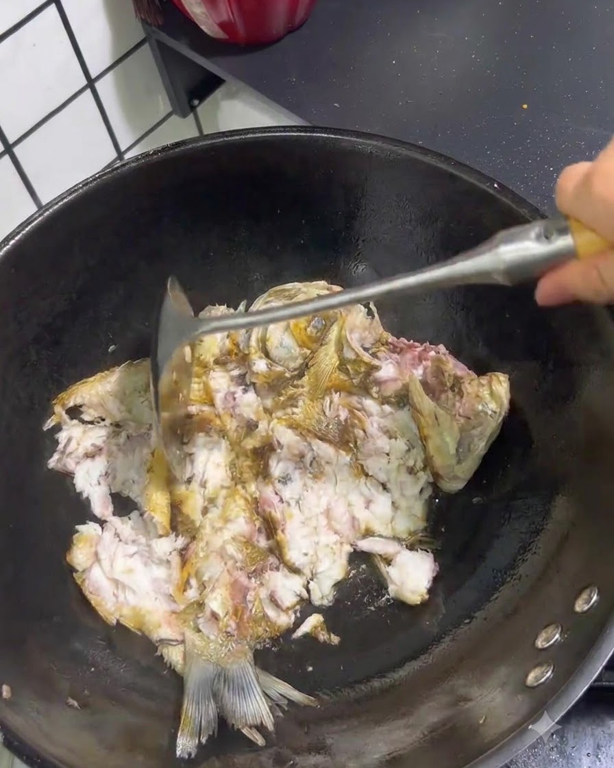 中華鍋の中で、金属製のスパチュラを使って焼いた魚を砕き、バラバラにしている様子。