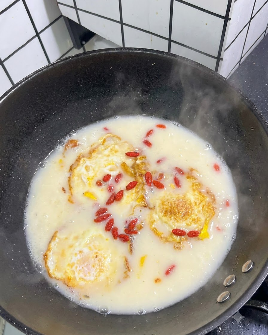 目玉焼きが入った白いスープの表面に、乾燥した赤いクコの実を散らしている様子。