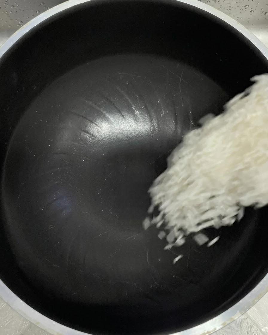 計量カップから黒い炊飯器の内釜へ白い米粒が落ちている様子。