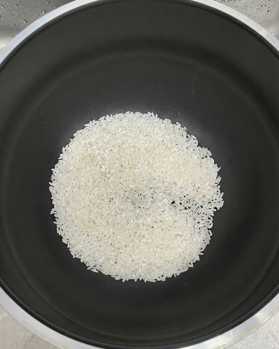 黒い鍋の底に白米が集まり、すすぎ用の水が加えられている様子。