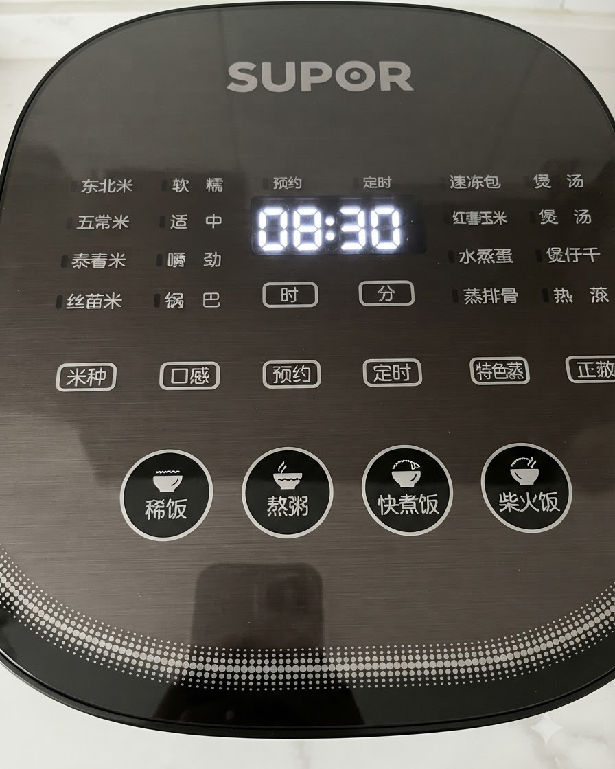 時間が表示された黒いデジタル炊飯器の操作パネルのボタンを、手が押しているクローズアップ。