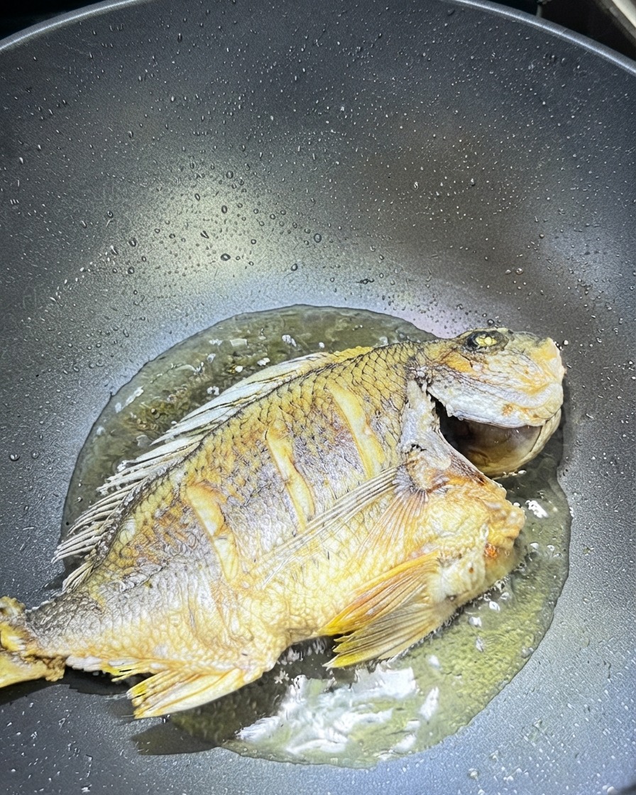フライパンの中で、焼かれた魚の周りに散らされたスライス生姜とにんにく。