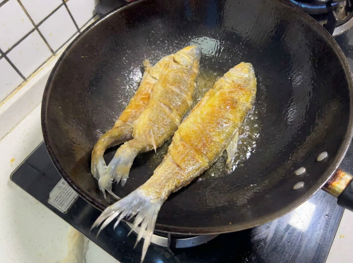 中華鍋の熱い油の中で、美味しそうなきつね色の焼き色をつけながら揚がっている2尾の魚。