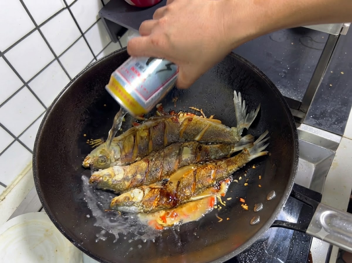 味付けされた揚げ魚と香味野菜が入った中華鍋に、ビールの缶からビールが注がれている様子。