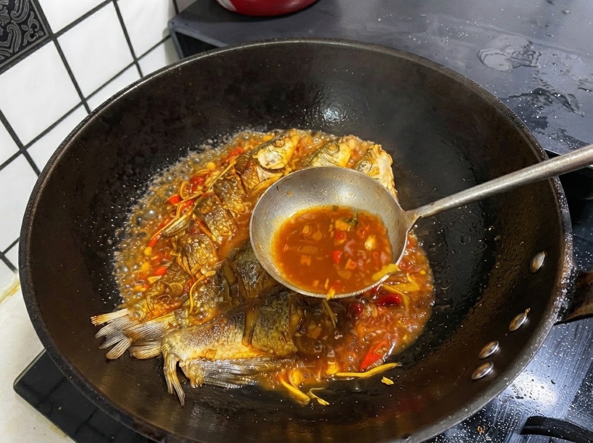 全体が丸ごと揚がった魚が入った鍋から、金属製のおたまですくい上げた濃厚な色の煮汁。