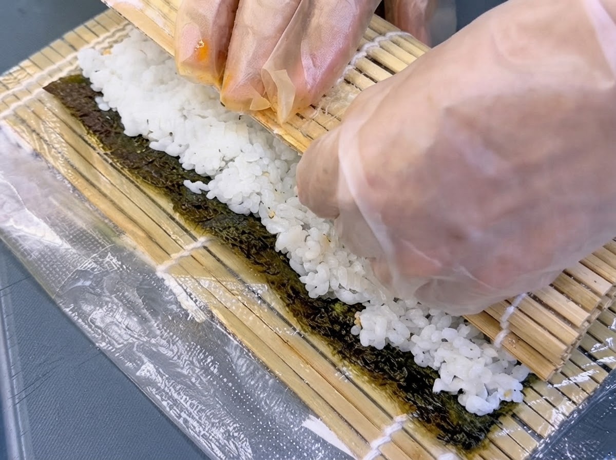 巻きすを使って手前からきっちりと海苔巻きを丸めている手元