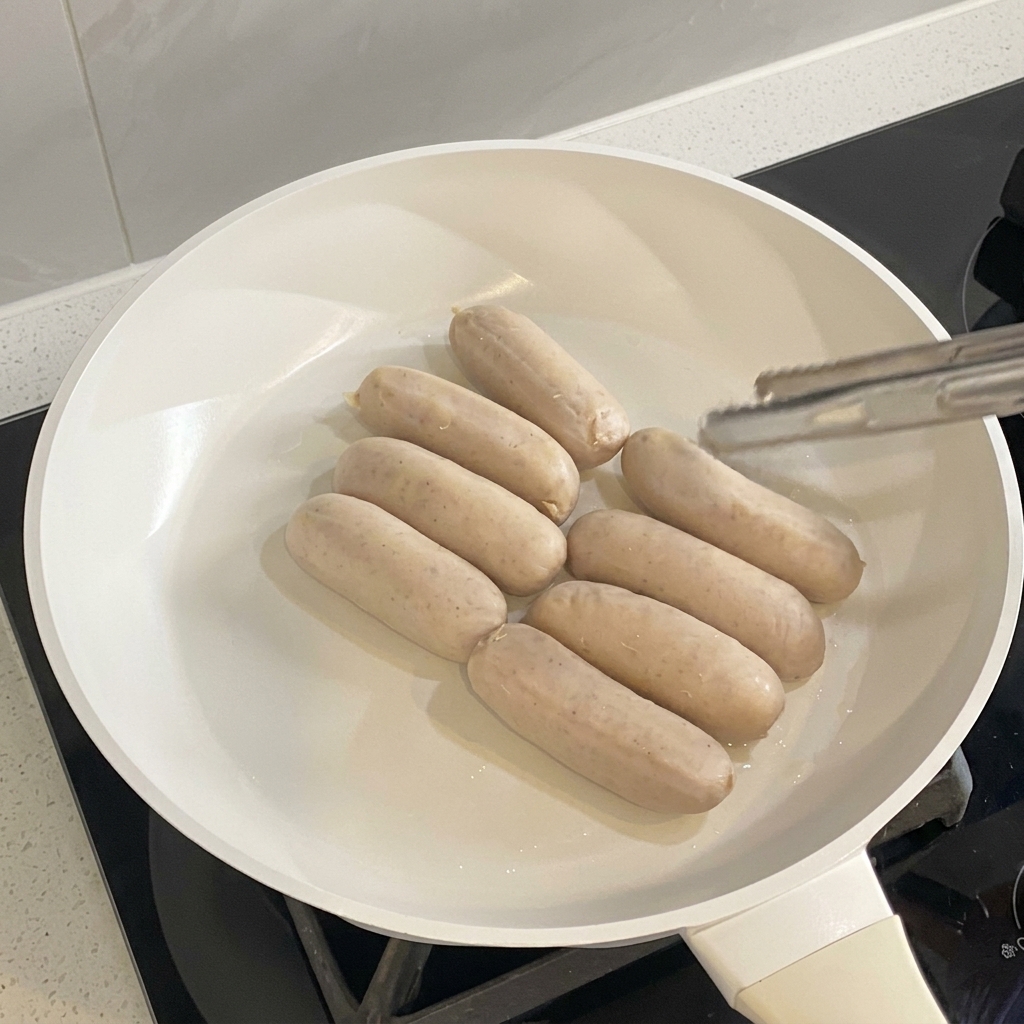 白いフライパンでソーセージが均一にきつね色に焼けている様子。