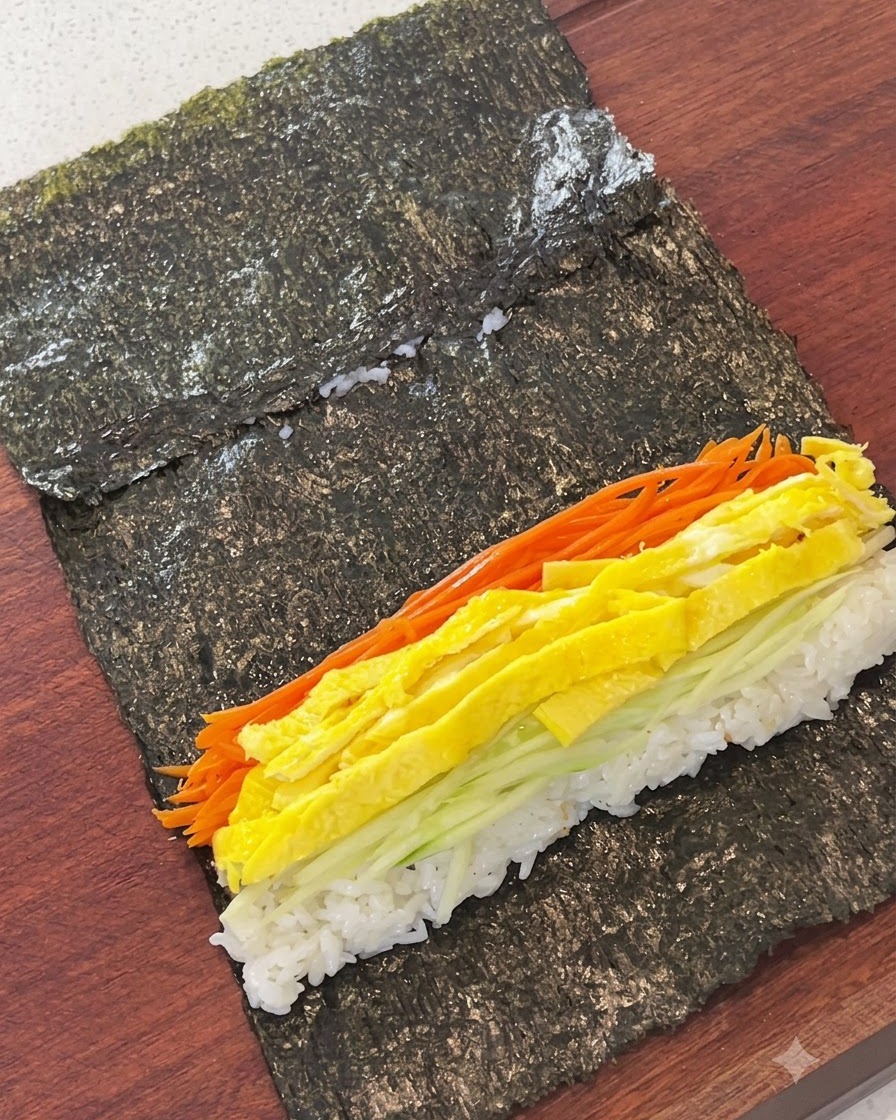 海苔の上に敷いたご飯の上に、千切りニンジン、卵、きゅうり、練り物が並べられている様子。