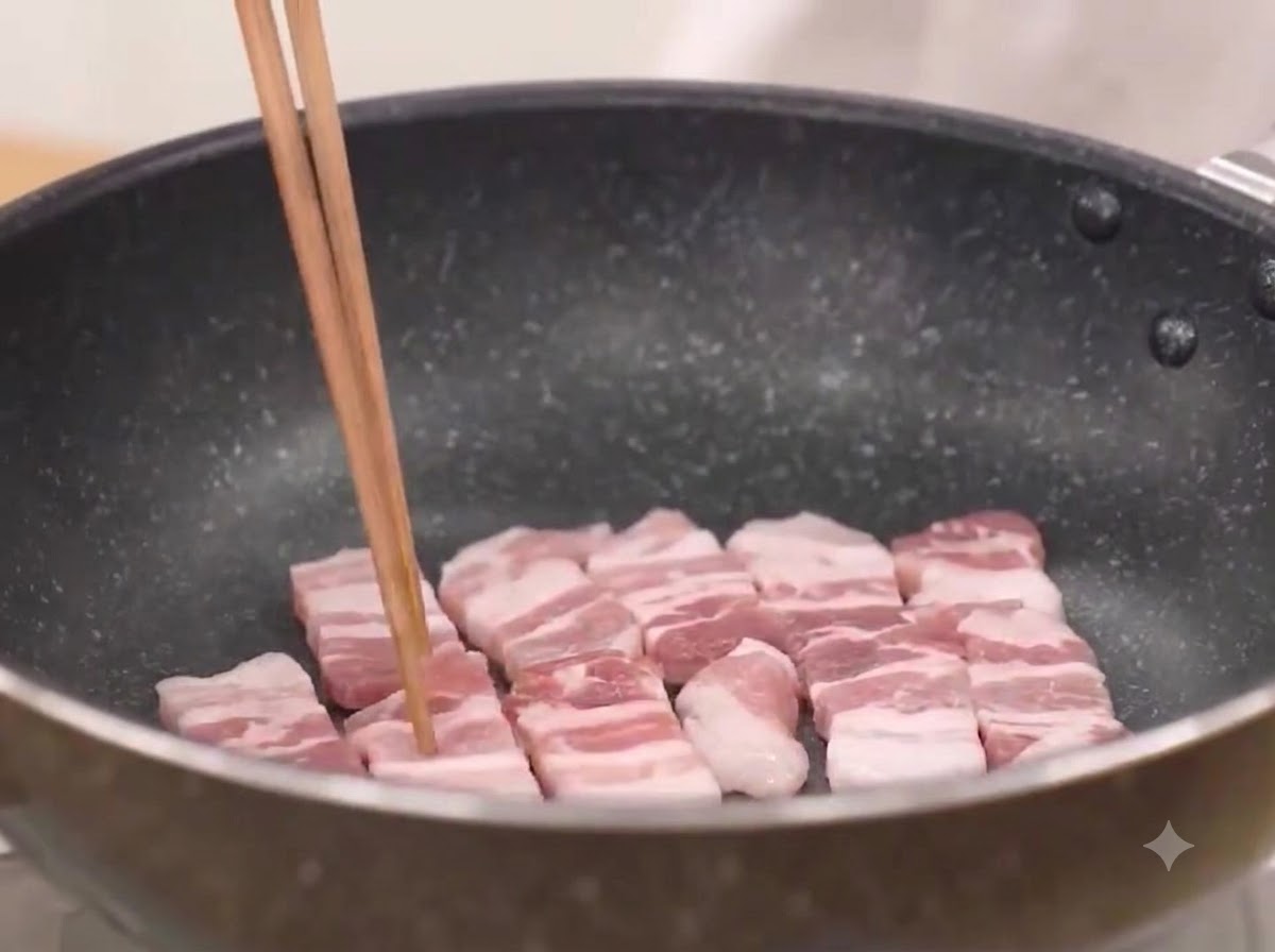 熱したフライパンで豚バラ肉をジュージューと炒めている様子